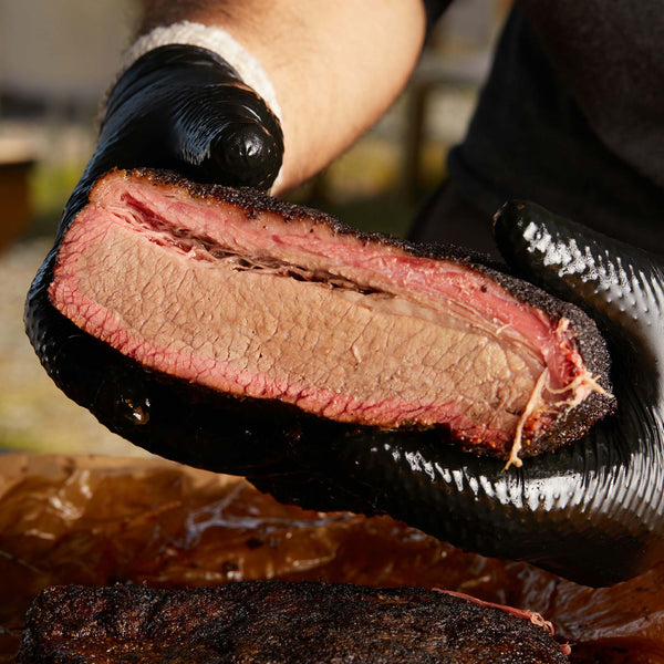 A person holding up a cross-section of cooked brisket.