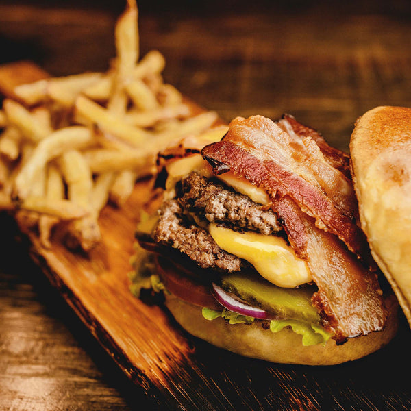 Side shot of prepared burger, sitting on a wooden cutting board with french fries.