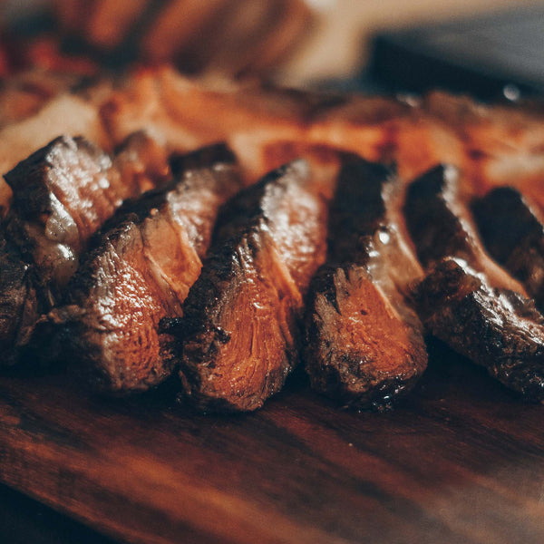 Slices of cooked flank steak resting on a wooden cutting board.