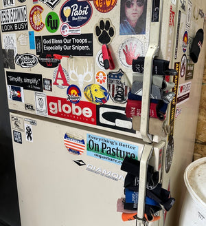 a shop beer fridge covered in stickers and stocked with Koozies in the door handle